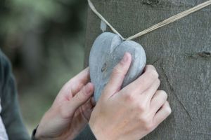 Angehörige hängt ein Holzherz an einen Baum